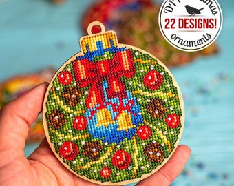 May include: A round wooden Christmas ornament with a green, red, and blue design. The ornament features a wreath with a red bow, bells, and pine cones. The text "DIY Christmas 22 DESIGNS! ornaments" is printed on a white circle.