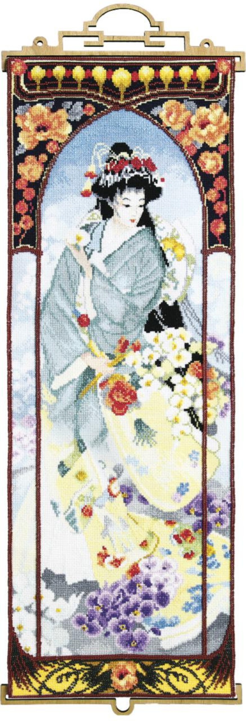Op de afbeelding: Een ingelijst borduurwerk met kruissteek, waarop een vrouw in een blauwe en witte kimono te zien is die een boeket bloemen vasthoudt. Het borduurwerk is omgeven door een decoratieve rand met bloemmotieven.