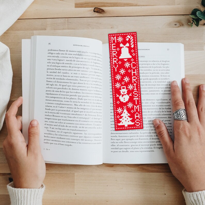 May include: Red and white Christmas bookmark with a snowman, a Christmas tree, and a bell. The bookmark says "Merry Christmas" in white letters.
