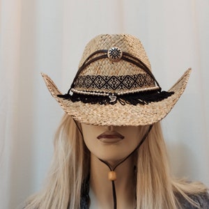 May include: A straw cowboy hat with a black and white geometric band, a silver sun charm, and black fringe trim.
