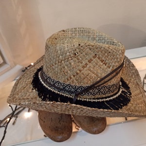 May include: A straw cowboy hat with a black and white patterned band and black fringe.