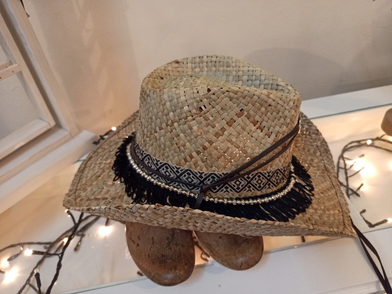 May include: A straw cowboy hat with a black and white patterned band and black fringe.