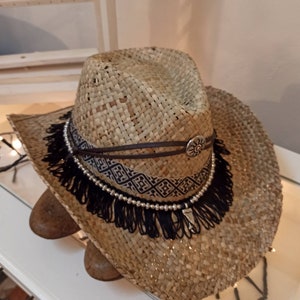 May include: A straw cowboy hat with a black fringe trim and a brown leather band with a silver sun design.