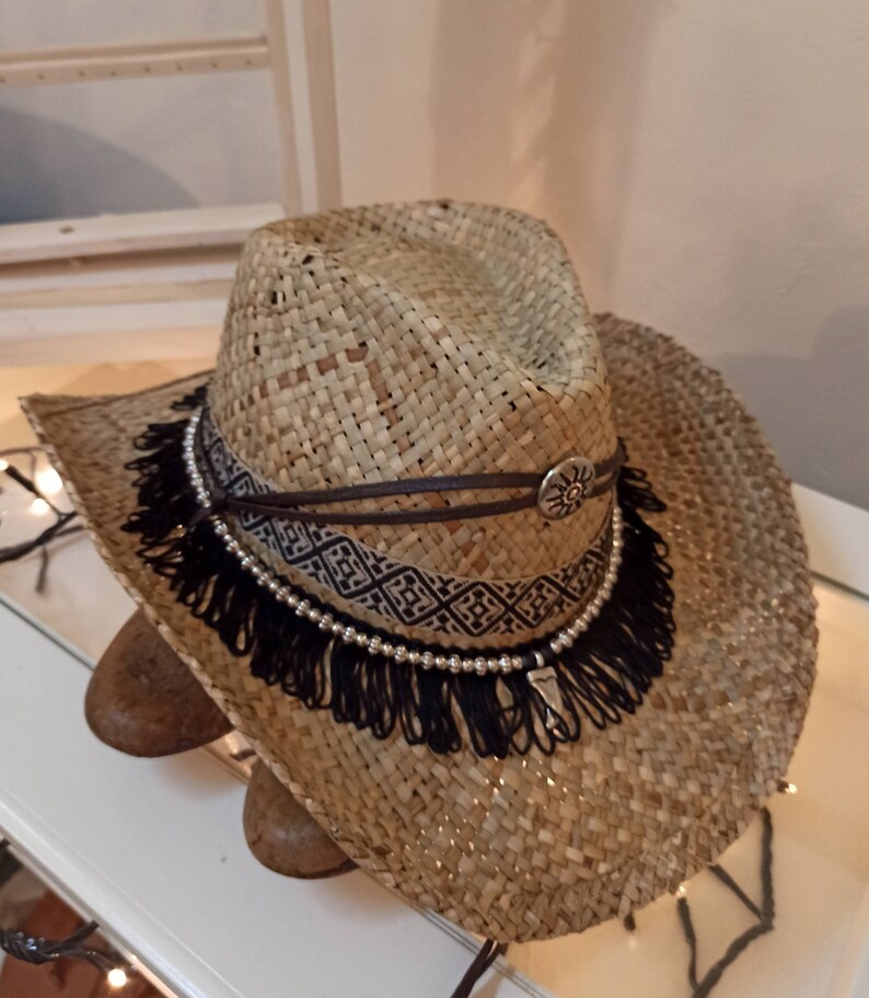 May include: A straw cowboy hat with a black fringe trim and a brown leather band with a silver sun design.
