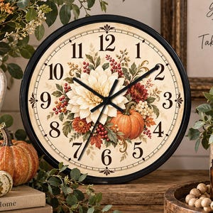 May include: A round wall clock with a black frame and a cream-colored face featuring black numerals. The center displays a floral arrangement with a large white dahlia, an orange pumpkin, red berries, and autumn leaves.