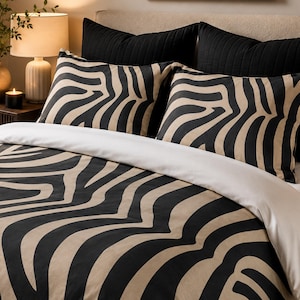 May include: A bedding set featuring a duvet cover and two pillow shams with a bold black and beige zebra stripe pattern. The duvet cover has a solid white top fold, and the pillow shams are positioned in front of two solid black quilted pillows.