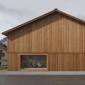 Könnte beinhalten: Ein modernes, hölzernes Gebäude mit einem großen Fenster. Das Gebäude ist aus hellbraunem Holz gebaut und hat ein schlichtes, rechteckiges Design. Das Fenster befindet sich an der Vorderseite des Gebäudes und ist von einem Holzrahmen umgeben.