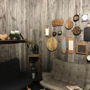 Puede incluir: Una sala de estar rústica con dos sofás grises y una estantería de madera con una olla de cobre y un melón. La pared está decorada con tablas de cortar de madera, un reloj y otros artículos de cocina.