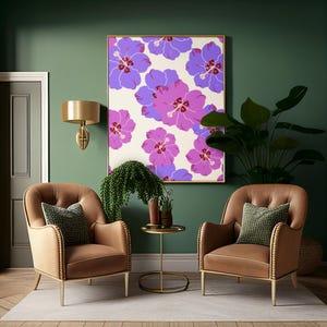 Op de afbeelding: Een ingelijste kunstprint met een herhalend patroon van paarse en roze hibiscusbloemen op een crèmekleurige achtergrond, geplaatst boven twee bruine gestoffeerde fauteuils met siernagels en donkergroene kussens.