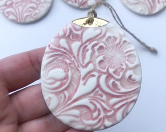 May include: Three pink and white ceramic ornaments with a floral pattern. The ornaments are round and have a gold loop at the top.