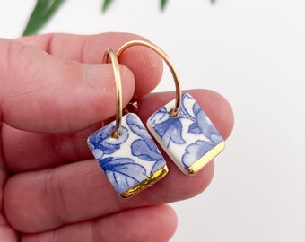 May include: A pair of gold hoop earrings with blue and white porcelain rectangular charms. The charms have a gold trim.