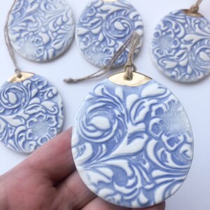 May include: Five blue and white ceramic ornaments with a gold rim and a floral pattern. Each ornament has a twine string for hanging.