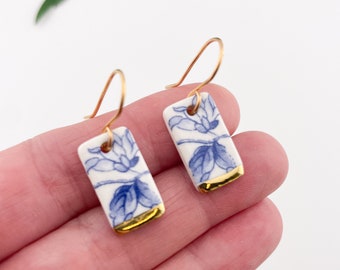 May include: A pair of blue and white porcelain earrings with gold trim. The earrings are rectangular in shape and feature a floral design.