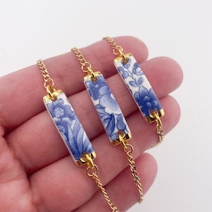 May include: Three gold chain bracelets with blue and white porcelain bar charms. The charms feature a floral pattern.