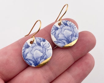 May include: A pair of blue and white porcelain earrings with gold accents. The earrings are round and feature a floral design.