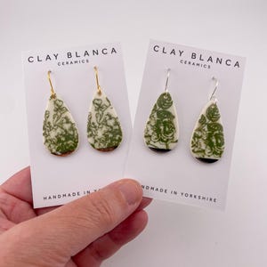 Op de afbeelding: Twee paar druppelvormige keramische oorbellen met een groen bloemmotief op een crèmekleurige achtergrond. De oorbellen worden gepresenteerd op witte kaarten met de tekst "CLAY BLANCA CERAMICS" en "HANDMADE IN YORKSHIRE".