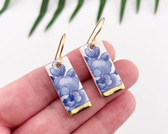 May include: A pair of blue and white porcelain earrings with gold accents. The earrings are rectangular in shape and feature a floral design.