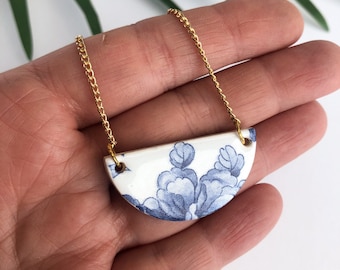 May include: A gold chain necklace with a white ceramic pendant featuring a blue and white floral design.
