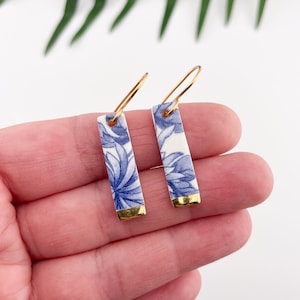Peut inclure: Une paire de boucles d'oreilles en porcelaine bleu et blanc avec des accents dorés. Les boucles d'oreilles sont de forme rectangulaire et présentent un motif floral.