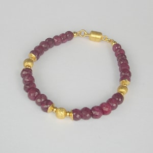 Peut inclure: Un bracelet en perles dorées et bordeaux avec un fermoir magnétique. Le bracelet est composé de petites perles bordeaux facettées et de plus grosses perles dorées à surface texturée.