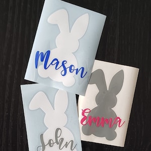 May include: Three bunny-shaped decals with names. One white bunny has the name "Mason" in blue script. Another white bunny has the name "John" in gray script. A gray bunny has the name "Emma" in pink script.