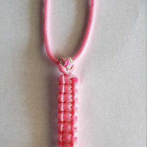 May include: Pink lanyard with a woven design, featuring a silver-colored clasp. The lanyard has a pink ribbon with a heart-shaped charm with a pink ribbon design. The lanyard is approximately 18 inches long.