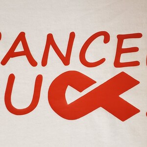 May include: White fabric with the words "CANCER SUCKS" in red, stylized lettering. The word "SUCKS" is partially replaced by a red awareness ribbon.