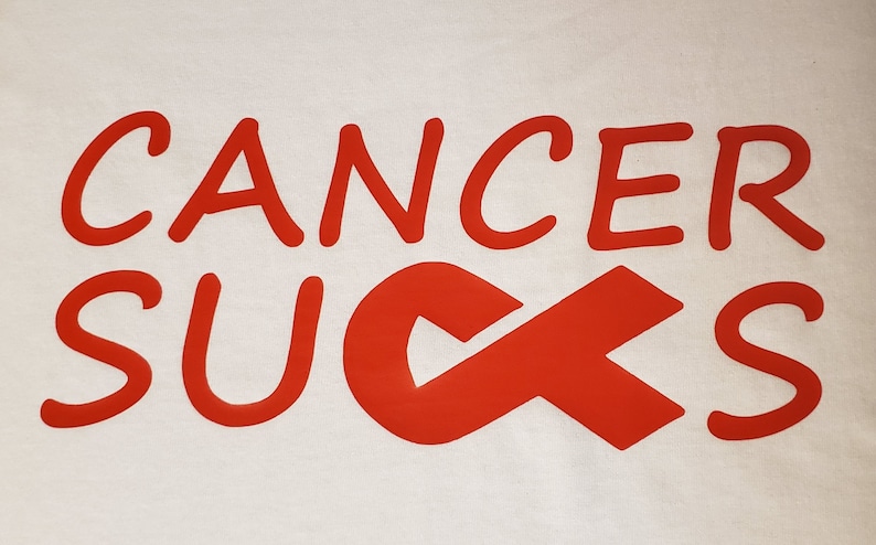 May include: White fabric with the words "CANCER SUCKS" in red, stylized lettering. The word "SUCKS" is partially replaced by a red awareness ribbon.
