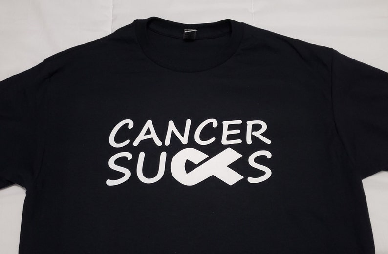 May include: Black t-shirt with the words "CANCER SUCKS" in white, along with a white awareness ribbon. The shirt is made of a soft material and has a crew neck.
