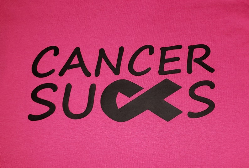 May include: A hot pink t-shirt with the words "CANCER SUCKS" in black, along with a black awareness ribbon. The text is in a bold, rounded font.