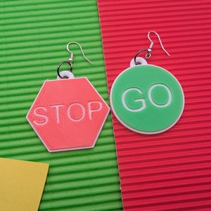 Puede incluir: Un par de pendientes con un octógono rojo con la palabra "STOP" y un círculo verde con la palabra "GO".
