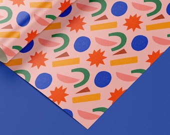 May include: Pink wrapping paper with a repeating pattern of green, blue, orange, and red geometric shapes. The shapes include stars, half circles, and curved lines.