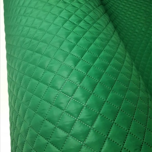 Pode incluir: Tecido verde acolchoado com um padrão de diamante. O tecido é liso e tem um leve brilho.