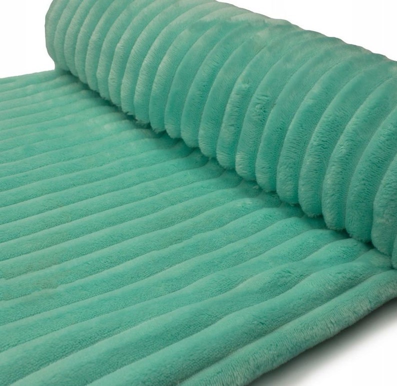 May include: A roll of soft, mint green corduroy fabric. The fabric has a ribbed texture with vertical lines. The material is plush and appears to be a medium weight. The fabric is rolled up on one end.