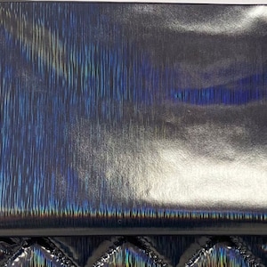 Op de afbeelding: Een close-up van een iriserende zilveren stof met een subtiel verticaal patroon. De stof heeft een metallic glans en een licht getextureerd oppervlak.