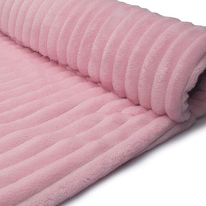 May include: A rolled-up section of soft, pink corduroy fabric. The fabric has a ribbed texture, with vertical lines running along its length. The material appears plush and fluffy, suggesting a cozy texture. The color is a light, pastel pink.