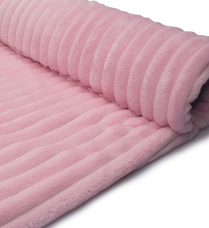 May include: A rolled-up section of soft, pink corduroy fabric. The fabric has a ribbed texture, with vertical lines running along its length. The material appears plush and fluffy, suggesting a cozy texture. The color is a light, pastel pink.