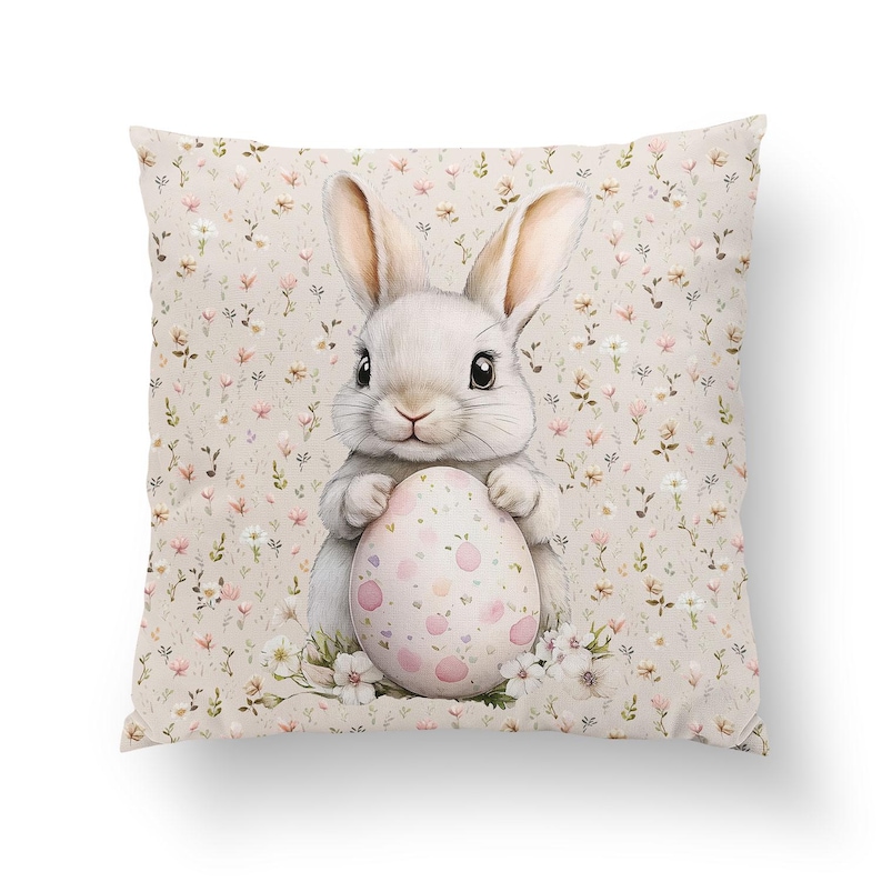 Pode incluir: Um coelho branco segurando um ovo de P&aacute;scoa rosa e branco com bolinhas. O coelho est&aacute; sentado em um fundo bege com um padr&atilde;o floral.