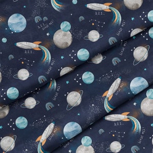 Pu&ograve; includere: Un tessuto blu navy con un motivo ripetuto di pianeti, stelle, arcobaleni e razzi. Il testo "3,2,1... blast off!" &egrave; ripetuto in tutto il motivo.