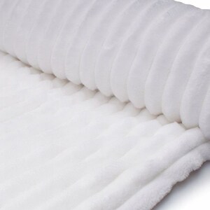 May include: A rolled-up, white, plush fabric with a ribbed texture. The soft material is a solid white color, and the ridges run parallel to each other, creating a pattern. The fabric appears to be a blanket or throw.