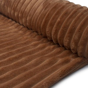 May include: Close-up of a rolled-up brown corduroy fabric. The fabric has a soft, plush texture with vertical ridges. The color is a warm, earthy brown, and the fabric appears to be thick and durable, suitable for upholstery or clothing.