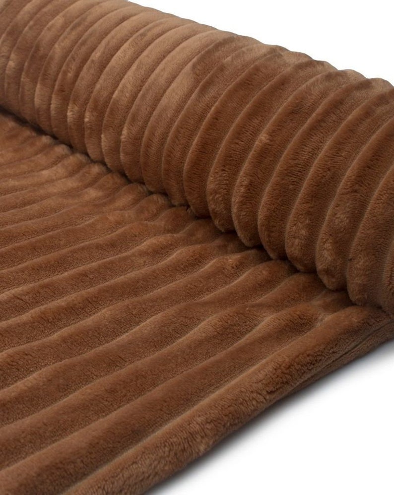 May include: Close-up of a rolled-up brown corduroy fabric. The fabric has a soft, plush texture with vertical ridges. The color is a warm, earthy brown, and the fabric appears to be thick and durable, suitable for upholstery or clothing.