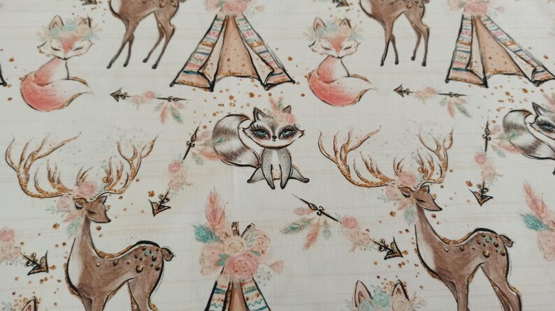 May include: A white fabric with a repeating pattern of woodland animals, including foxes, raccoons, and deer. The animals are surrounded by floral designs, arrows, and teepees. The fabric has a subtle glitter effect.