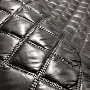 Op de afbeelding: Zwarte quilted stof met een ruitpatroon. De stof heeft een glanzende, bijna metallic afwerking.
