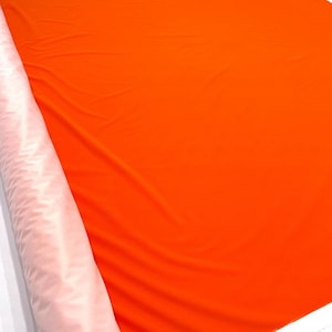 Może przedstawiać: Rolka jasno pomarańczowej tkaniny prezentowana na białym tle.