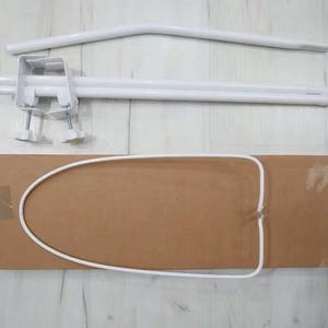 Puede incluir: Un marco de dosel para cuna de bebé de metal blanco con dos postes ajustables y un aro de metal blanco. El marco está ensamblado en una caja de cartón marrón.