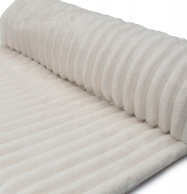 May include: A roll of off-white, ribbed fabric. The fabric has a soft, plush texture and a corduroy-like appearance. The ribbed pattern runs lengthwise, creating a series of parallel lines across the surface.