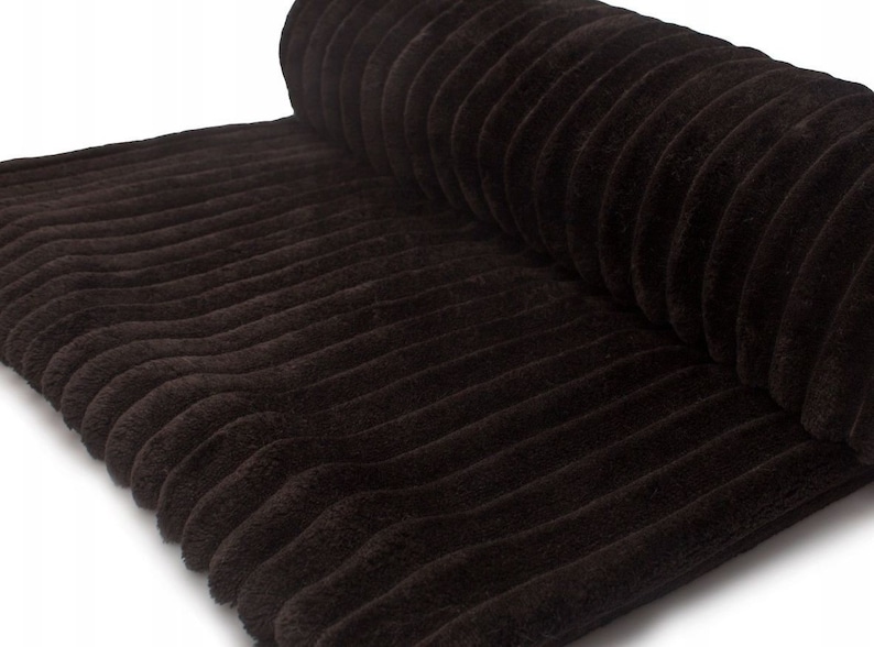 May include: A roll of dark brown corduroy fabric. The fabric has a ribbed texture with vertical lines. The corduroy is a soft, plush material, and the roll is partially unrolled, revealing the texture.