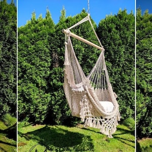 May include: A beige hammock chair with fringe hanging from a wooden frame in a backyard setting. The chair is made of woven rope and has a white and gray patterned cushion.