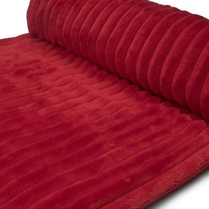 May include: A rolled-up, plush red fabric with a ribbed texture. The fabric is a solid, vibrant red color and appears soft and inviting. The ribbed pattern runs lengthwise across the material, creating a visually interesting surface.